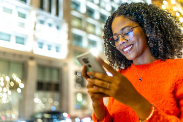 Smiling young woman using smartphone on city street at night