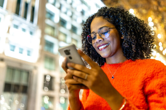 Smiling young woman using smartphone on city street at night