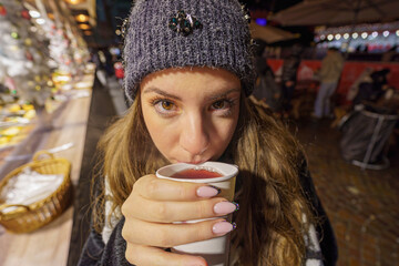 Young girl drinks wine and looks into the camera at an advent fair