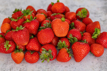Pile of fresh organic strawberries with vibrant red color and green leaves on a light stone surface, showcasing healthy eating, summer harvest, and natural fruit freshness in detail