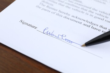Ballpoint pen leaving signature on contract at wooden table, closeup