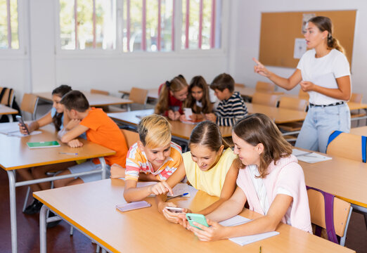 Group of kids using smartphones during lesson in school. Girls and boys using gadgets while studying.