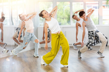 Young girl in bright clothes, together with group of teenage friends, learn to dance hip hop in...