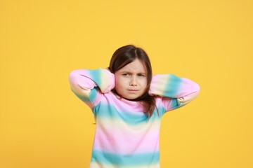Annoyed little girl covering her ears from loud sound on yellow background