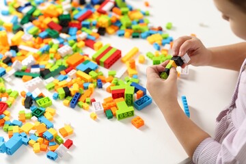 Girl playing with building blocks at white table indoors, closeup