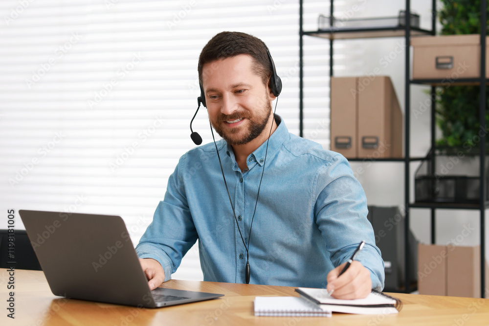 Poster interpreter in headset taking notes while having video chat via laptop at wooden table indoors