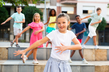 Obraz premium Modern preteen girl dancing with group of friends on city street. Urban lifestyle. Alpha generation..