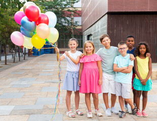 Full length portrait of multiracial group of happy preteen girls and boys with bunch of multicolored helium balloons in hands in city on summer day © JackF