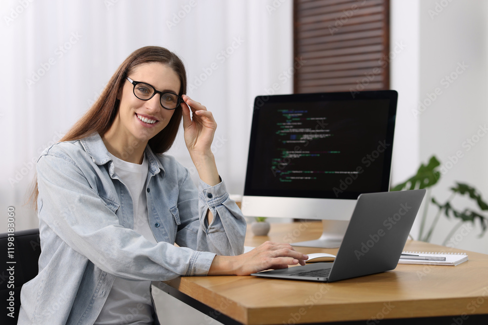 Poster programmer working on laptop and computer at wooden desk indoors