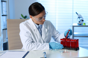 Laboratory testing. Doctor taking test tube with blood sample from rack at table indoors