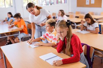 Friendly teacher woman helping children during lesson in the schoolroom