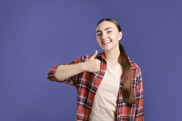 Fototapeta premium Happy woman showing thumbs up on purple background, space for text. Like gesture