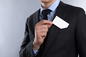 Man taking blank business card from pocket of his jacket on grey background, closeup. Mockup for design