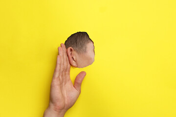 Man showing hand to ear gesture through hole in yellow paper, closeup