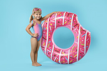 Cute little girl in beachwear with diving mask and inflatable ring on light blue background