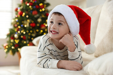 Happy little boy in Santa hat on sofa at home