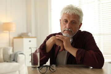 Sad senior man feeling lonely while sitting at wooden table indoors