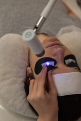 A woman undergoing eyelash extension procedure using an ultraviolet lamp.