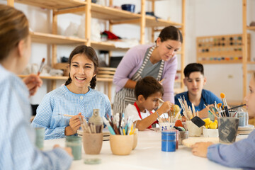 Positive preteen girl speaking to a circle member while processing ceramic items in workroom