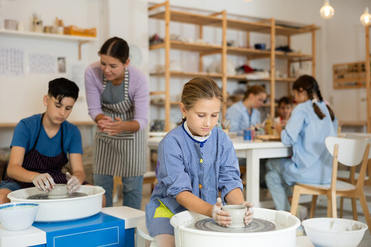 Pleased underage attendees of pottery circle working at throwing-wheel with female instructor