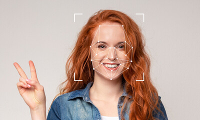 A young woman with vibrant red hair smiles widely while making a peace sign with her hand. Facial...