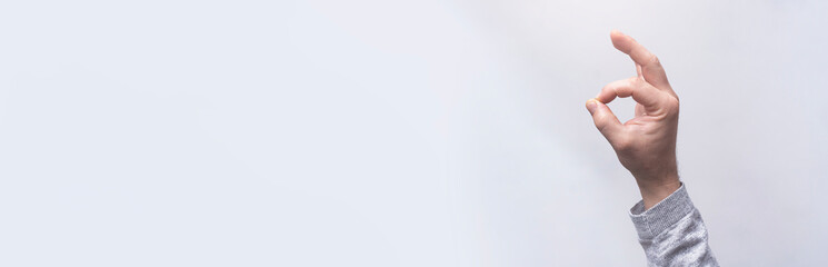 Close-up of a man in a shirt shows hand gesture OK against a gray wall.