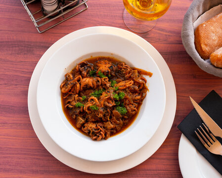 Mediterranean cuisine, mini octopuses with tomato sauce and onions in a white ceramic plate