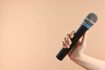 Woman with microphone on beige background, closeup. Space for text