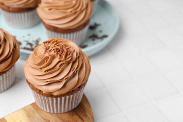 Tasty cupcakes with chocolate cream on white tiled table, closeup. Space for text