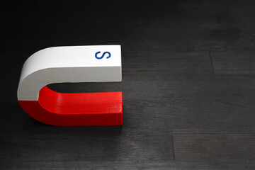One horseshoe magnet on black wooden table, space for text