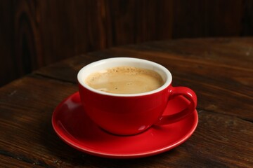 Red cup with coffee on wooden table, closeup