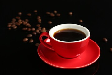 Red cup with coffee and roasted beans on black background, closeup