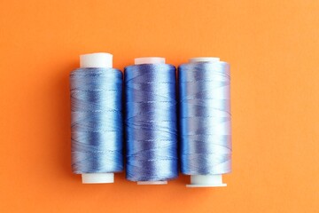 Spools of colorful sewing threads on orange background, flat lay