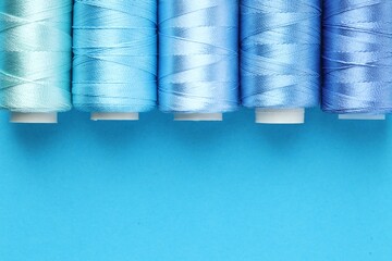 Spools of sewing threads on light blue background, flat lay. Space for text