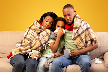 Flu season concept. Sick black parents and child girl feeling unwell, blowing runny noses and...