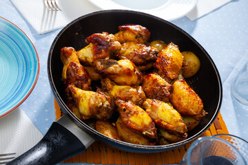 Appetizing crispy fried chicken wings with potatoes served in fry pan..