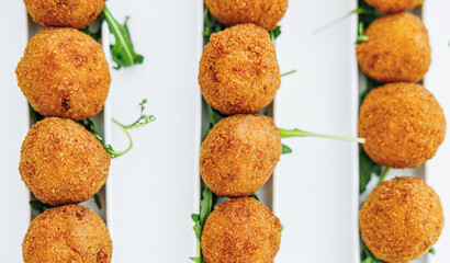 Overhead shot of a plate filled with neatly arranged arancini in three rows. This traditional Sicilian delicacy showcases culinary art and Mediterranean flavors, perfect for food lovers and culture en