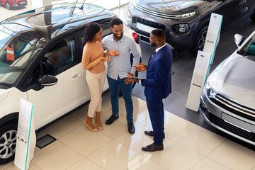 Salesperson In Modern In Dealership Center Consulting Young Black Spouses, African American Couple...