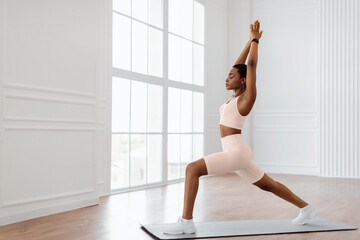 Yoga Training. Calm African American Lady Standing In 1 Warrior I Or Anjaneyasana Pose On Mat, Doing Forward Lunges Raising Arms Lifting Hands Up, Training At Home Or Fitness Studio, Free Copy Space