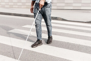 Unrecognizable young black man with vision disability walking across city street, using walking cane outdoors, copy space. Millennial blind guy crossing road alone, cropped view
