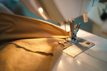 Close-up of a sewing machine needle and presser foot sewing beige fabric.