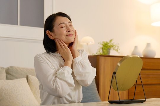 夜のリビングで顔に化粧水を塗る50代の女性