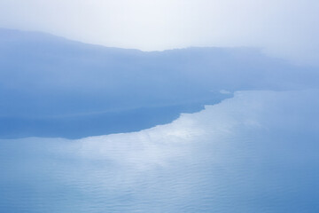 Misty coastal landscape with soft light reflecting on calm waters. A serene and minimalistic stock photo capturing tranquility of nature, featuring hazy horizons and gentle gradients of sea and sky