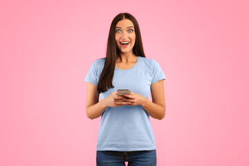 Surprised positive woman using smartphone device, chatting online, typing sms, glad to recieve many...