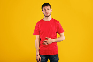 Pleasant Feeling In Stomach. Satisfied smiling young man keeping hand on belly, being in good mood after eating delicious meal, demonstrating that he is full, isolated over blue background