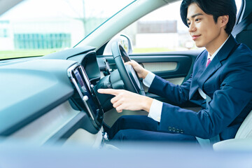 カーナビ、運転、ビジネスマン、男性、自動車、ナビゲーション、画面、操作、タッチパネル、ドライバー、ドライブ、クルマ、検索、ITS、ADAS、自動運転、タッチ、エレクトロニクス、電動、電子化、スーツ、笑顔、ダッシュボード、インパネ、インテリア、車内、ハンドル、シートベルト、安全、機能、メーター、ボタン、DX、IoT、テクノロジー、交通、日本人、運転手、運転席、安全運転、若い、旅行、外出、道路、道案内