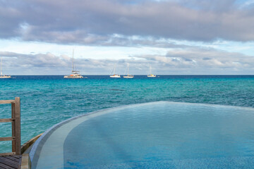 French Polynesia, Rangiroa Atoll. Infinity pool and sailboats on ocean.