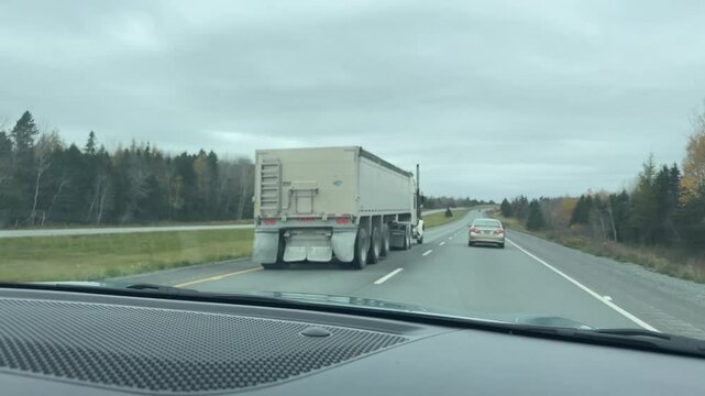 View from the front window of a car on a large semi-trailer truck overtaking on a highway in a rural area. Nova Scotia, Canada. An American truck overtakes a car on the highway.