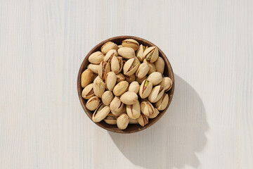 Pistachios in a wooden plate, on a light background.