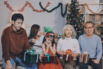 Portrait of Asian family exchanging presents during christmas at home. Attractive happy people holding gift box, celebrate holiday thanksgiving, xmas eve tradition in living room in house together.